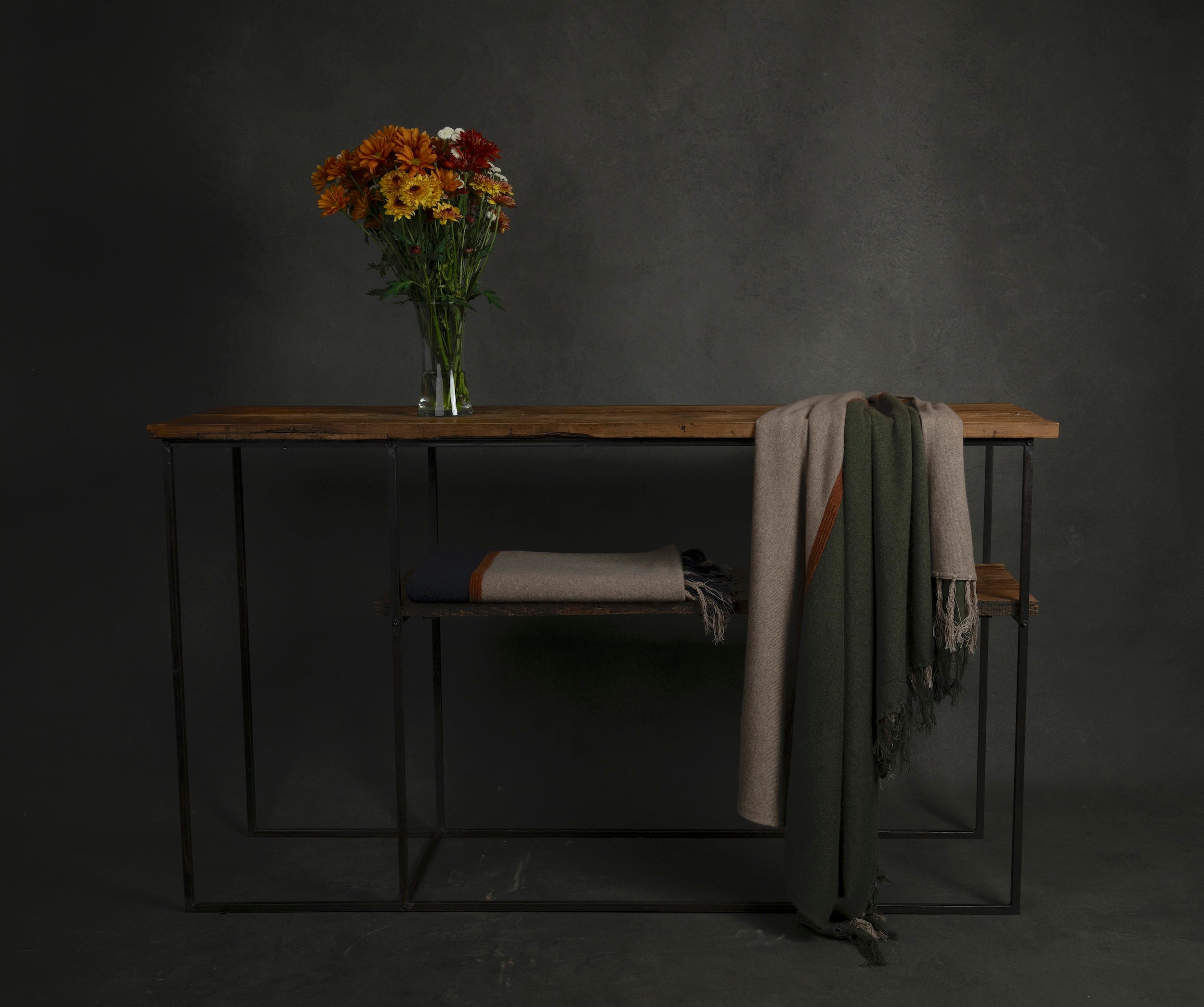 Wooden table with a vase of flowers and draped cloths against a dark background