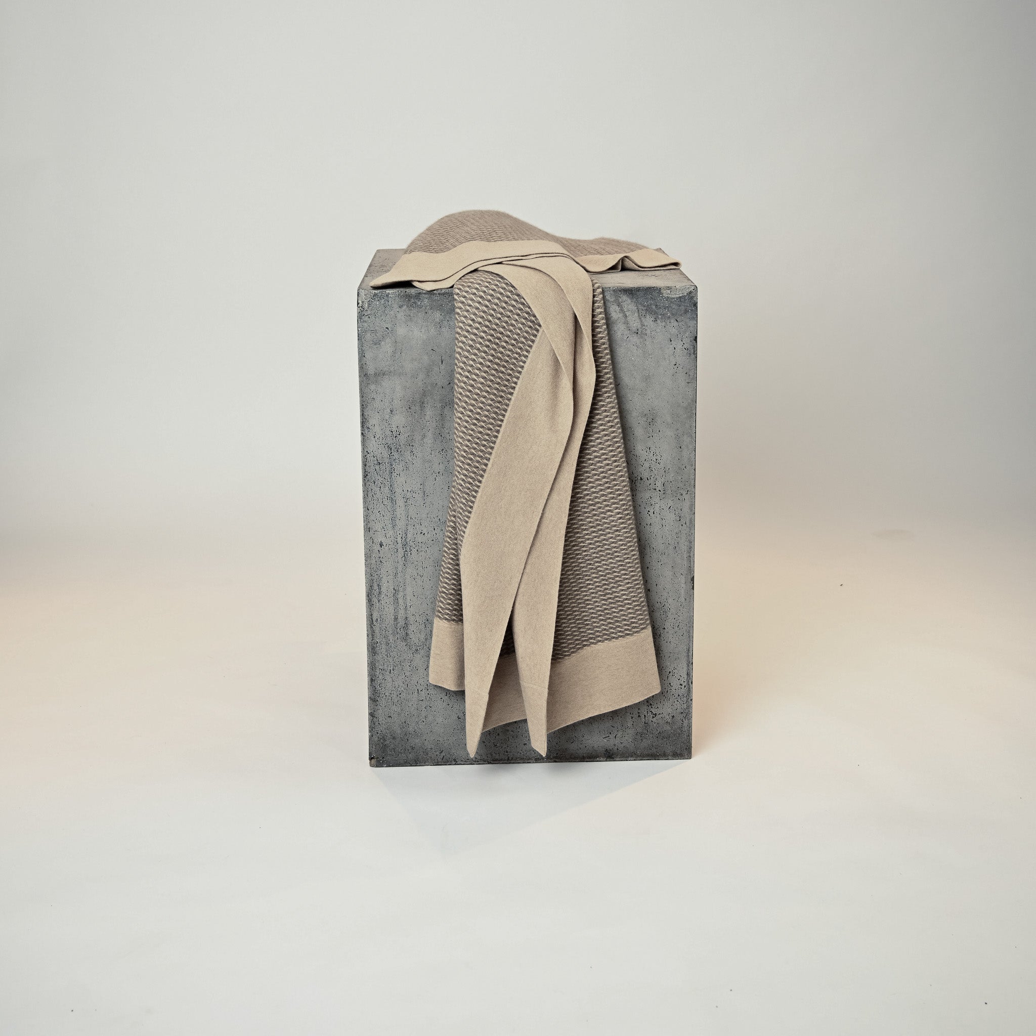 Beige blanket draped over a textured gray box on a light gray background